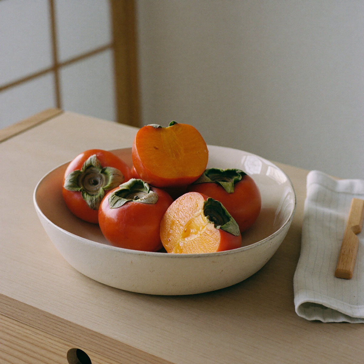Ripe kaki persimmons in a ceramic bowl on a wooden kitchen counter