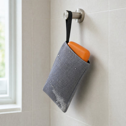 Grey exfoliating soap bag holding an orange Wakai bar, hanging from a shower hook